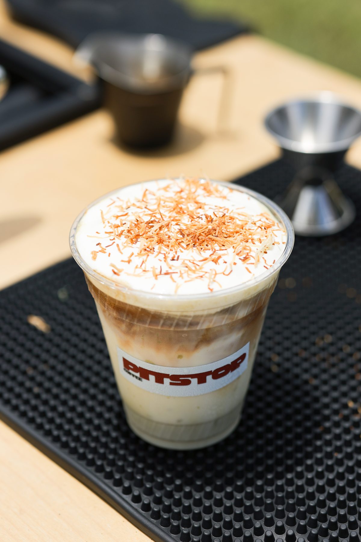 An iced latte topped with toasted coconut in a Pit Stop branded cup