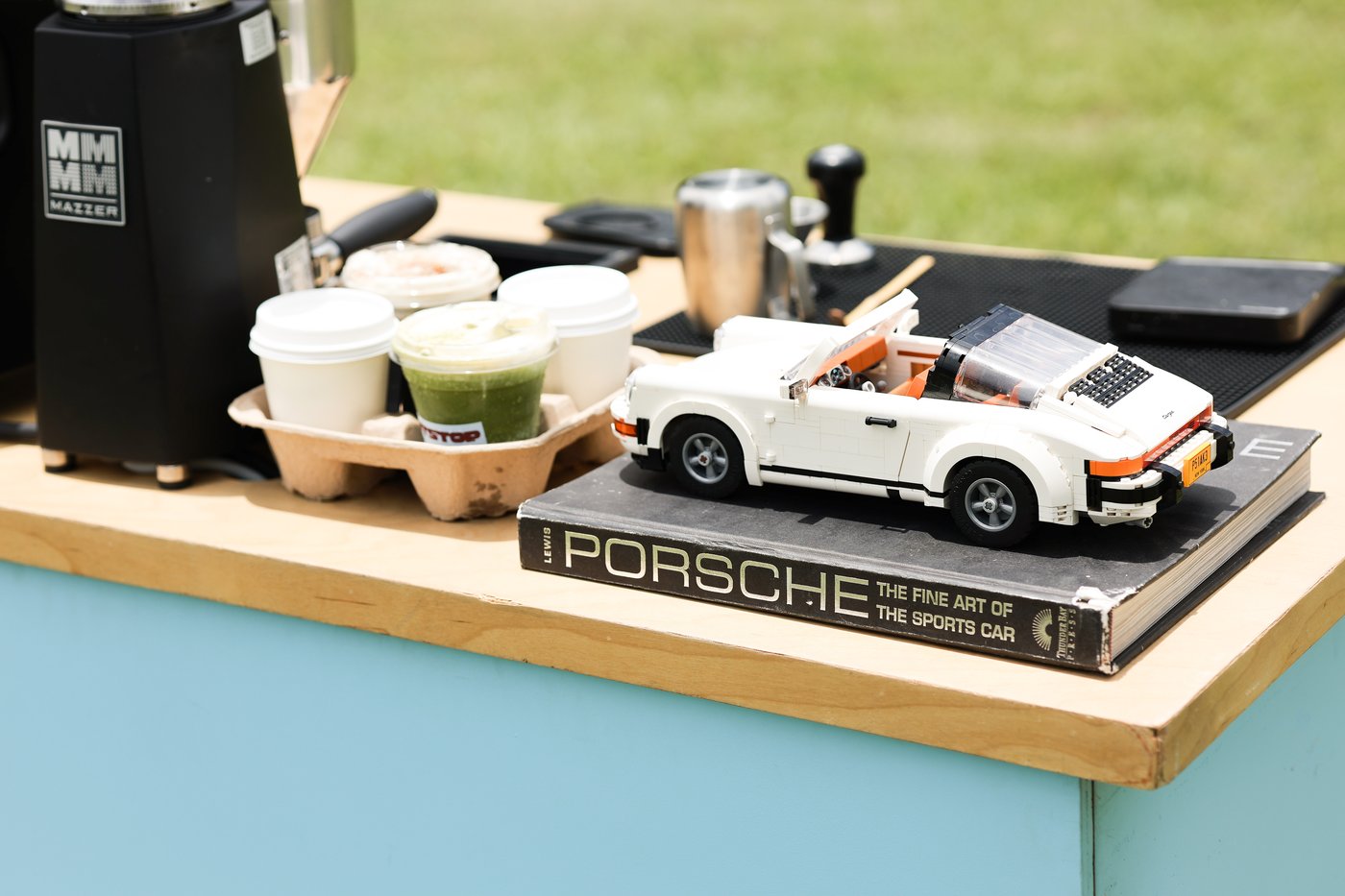 A Pit Stop iced coffee and matcha next to a model Porsche resting on a Porsche book, on the cart counter